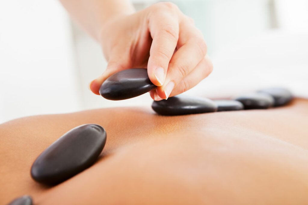 Massage therapist putting hot stone on person's back