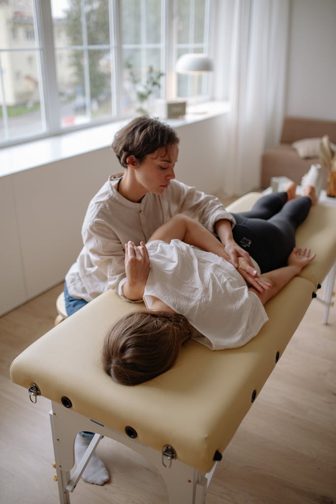 A Therapist Holding a Woman's Hand Lying on a Massage Table